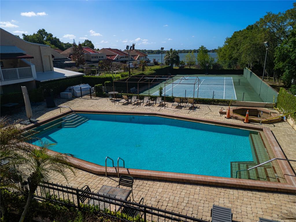 An outdoor swimming pool and tennis court are situated next to a lake — 4 CASARENA COURT, WINTER HAVEN, FL