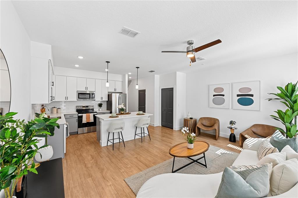 An open-concept kitchen and living area features white cabinetry, a kitchen island, and wood flooring — 1898 ZAC STREET UNIT Equinox, KISSIMMEE, FL