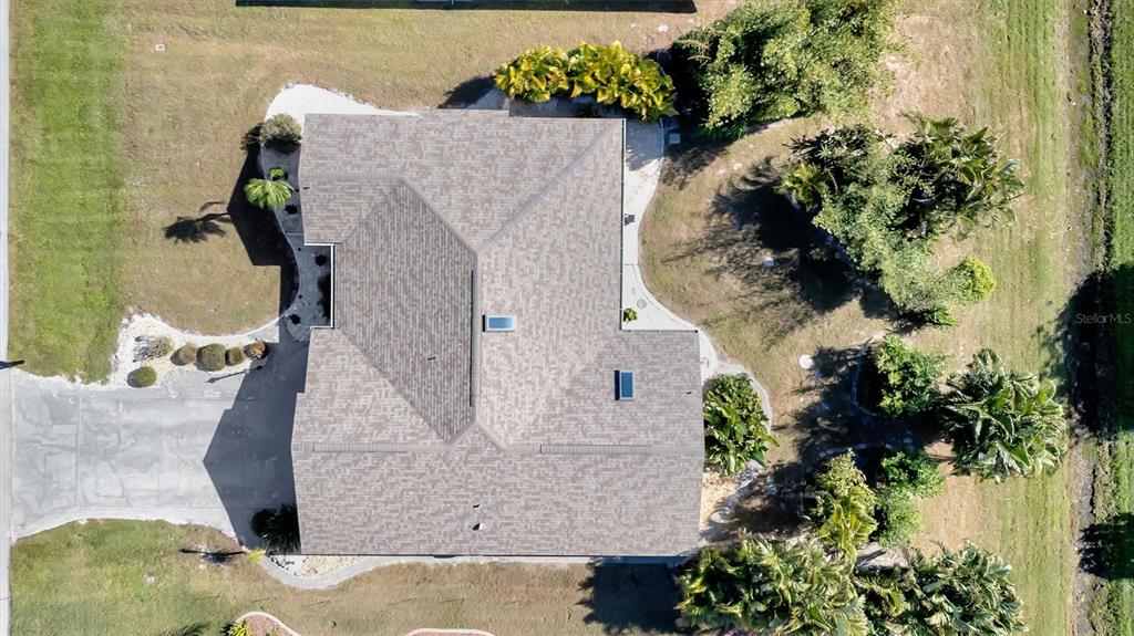 An aerial view shows a house with a shingled roof, two skylights, and surrounding landscaping — 27518 TIERRA DEL FUEGO CIRCLE, PUNTA GORDA, FL