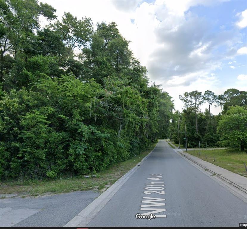 A paved road runs between a dense wooded area and an open grassy lot — Lot 10 NW 20TH AVENUE, OCALA, FL