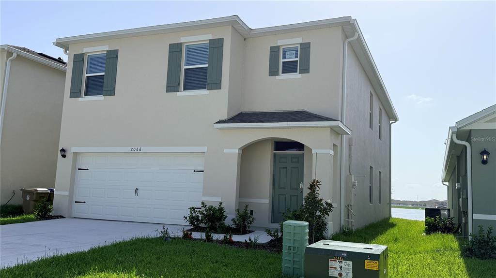 A two-story, beige stucco house features a two-car garage and a front-facing entrance — 2066 WALNUT CREEK DRIVE, KISSIMMEE, FL