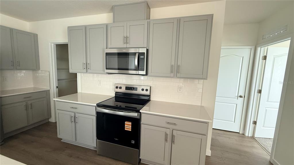 A kitchen features gray cabinets, white countertops, a subway tile backsplash, and stainless steel appliances — 2066 WALNUT CREEK DRIVE, KISSIMMEE, FL