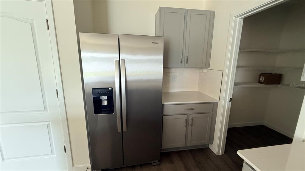 A kitchen features a stainless steel refrigerator, grey cabinets, white countertops, and an adjacent pantry — 2066 WALNUT CREEK DRIVE, KISSIMMEE, FL