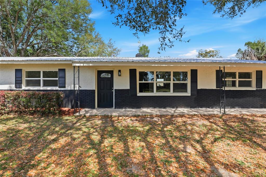 The exterior of a single-story house features a white stucco upper wall, black brick base, and metal roof — 980 SW 105TH STREET, TRENTON, FL
