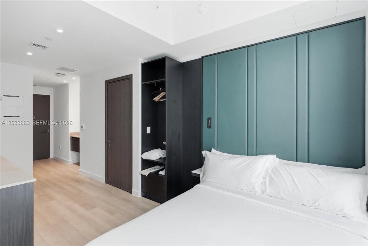 A modern bedroom features a teal paneled headboard, light wood flooring, and an open closet — 20 NE 11th # 4212, Miami FL 33132, MIAMI, FL