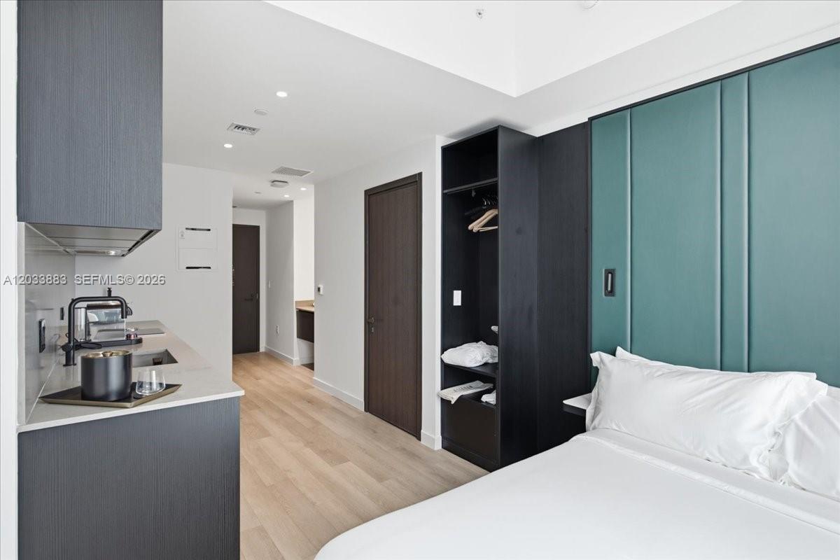 A modern studio apartment features a kitchenette, open closet, and a bed with a teal headboard — 20 NE 11th # 4212, Miami FL 33132, MIAMI, FL