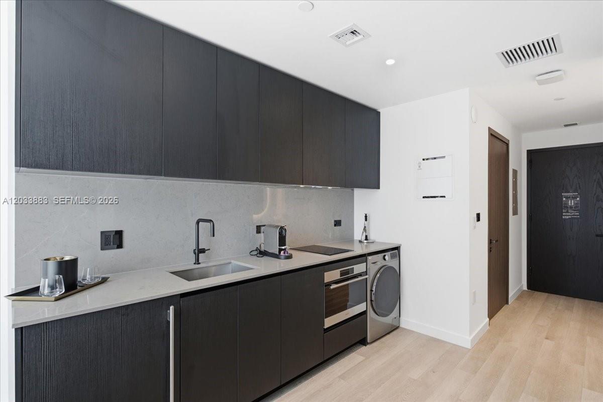 A modern kitchen features dark wood cabinetry, light stone countertops, and a built-in washing machine — 20 NE 11th # 4212, Miami FL 33132, MIAMI, FL