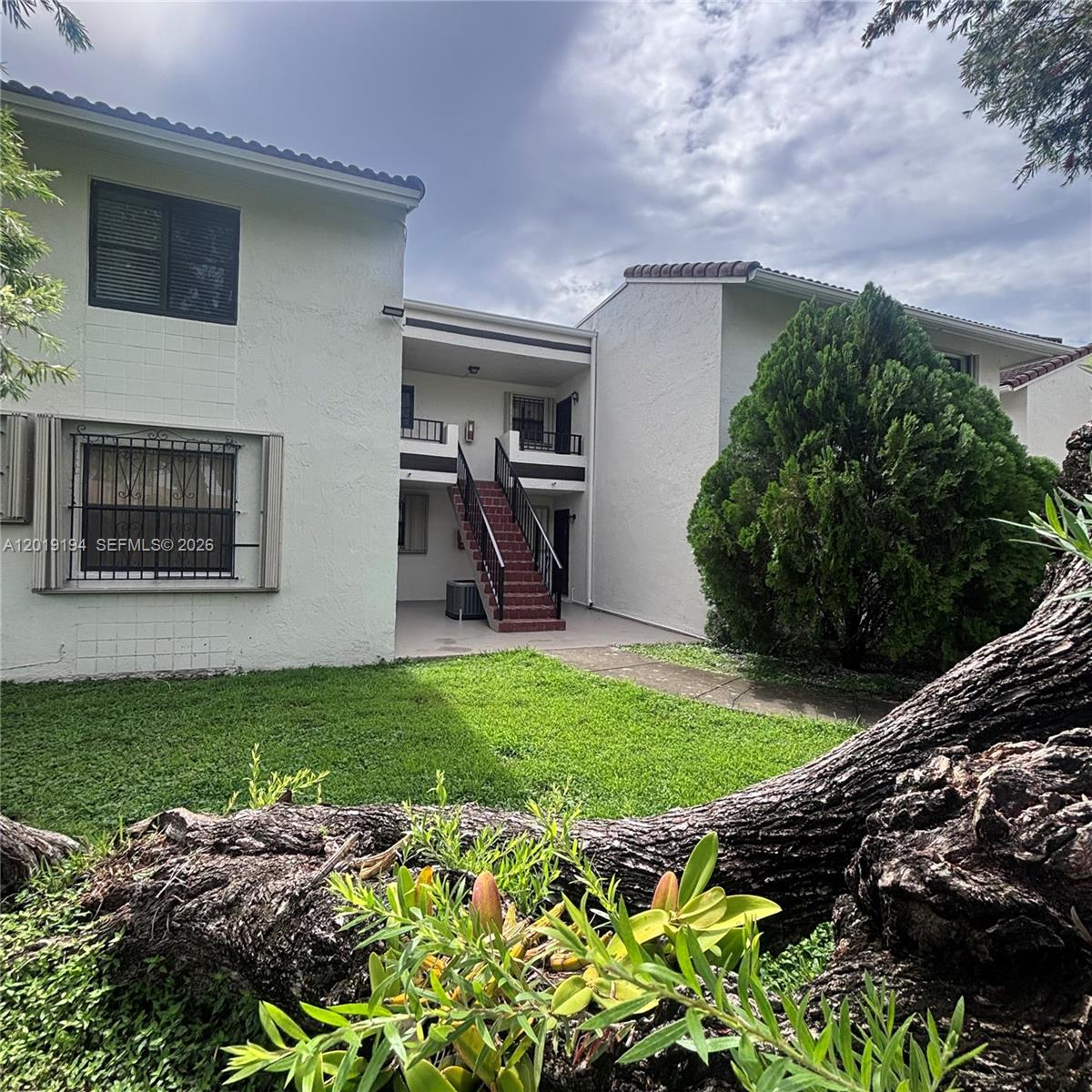 A two-story apartment building features a central outdoor staircase and a grassy front yard — MIAMI, FL