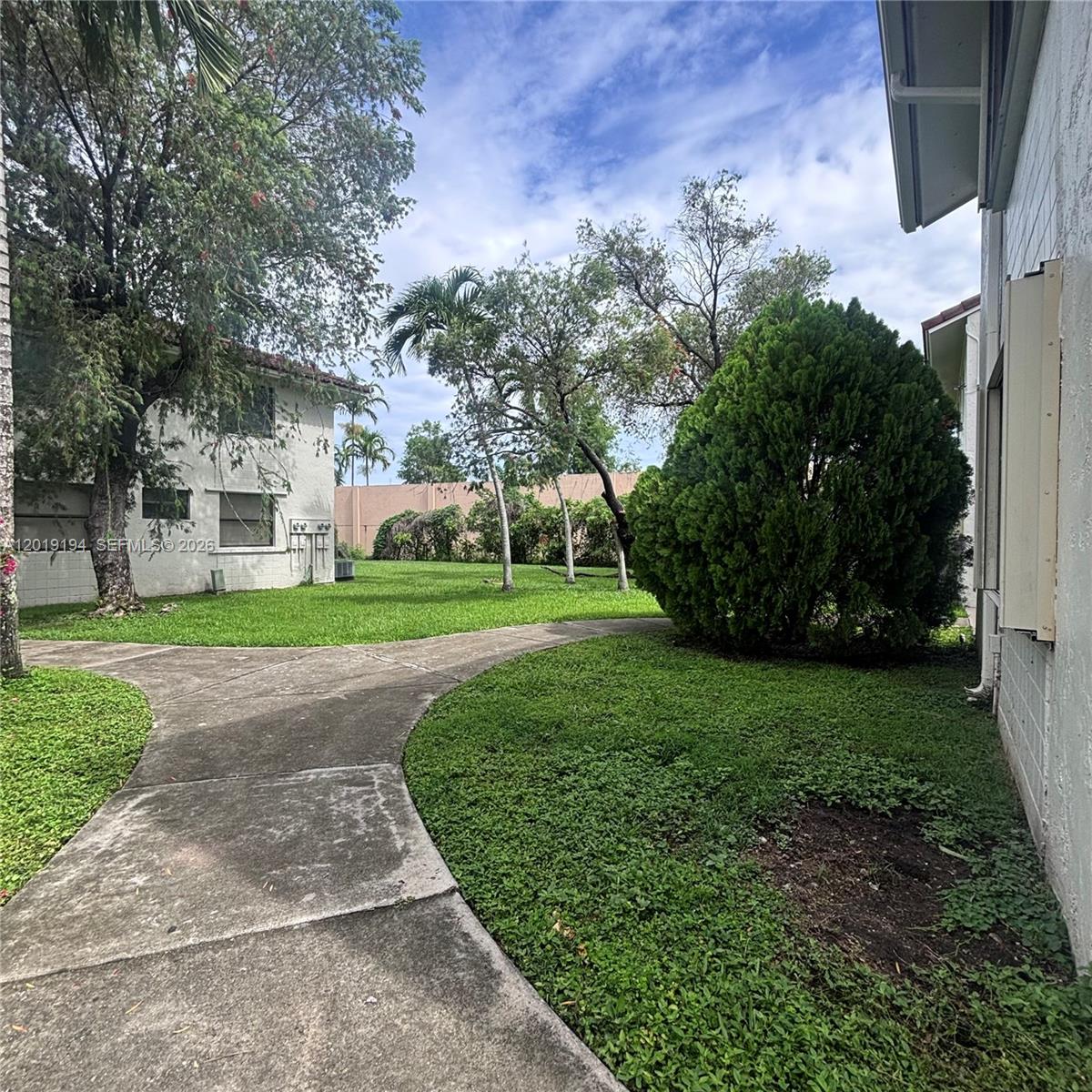 A concrete walkway winds through a grassy courtyard between two white residential buildings — MIAMI, FL