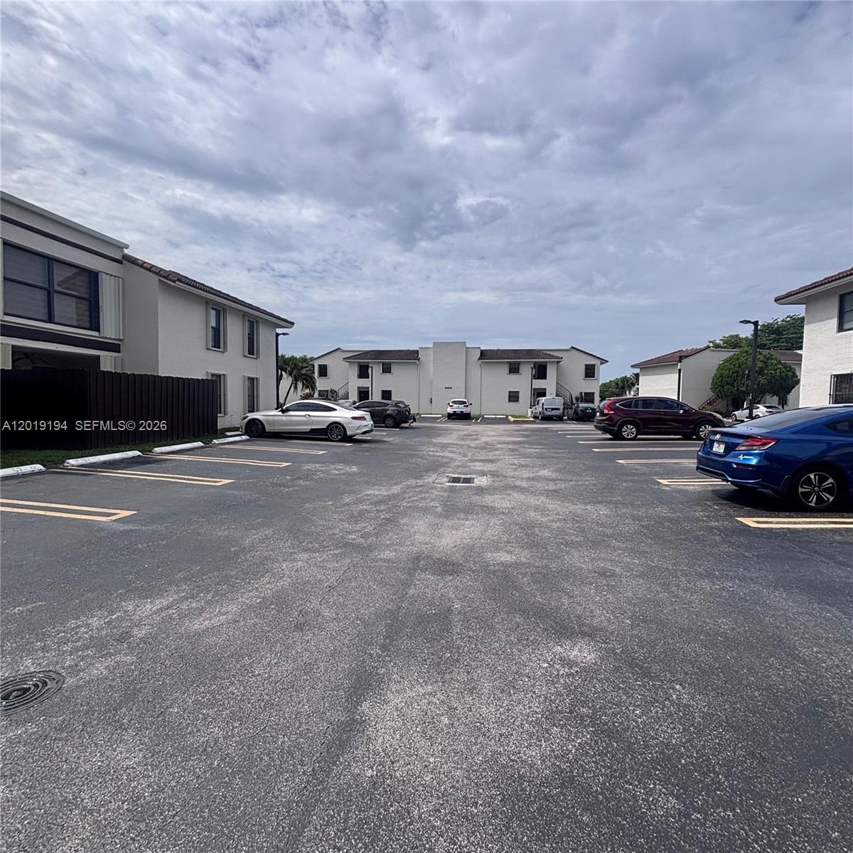 This exterior view shows a parking lot surrounded by multi-story apartment buildings under a cloudy sky — MIAMI, FL