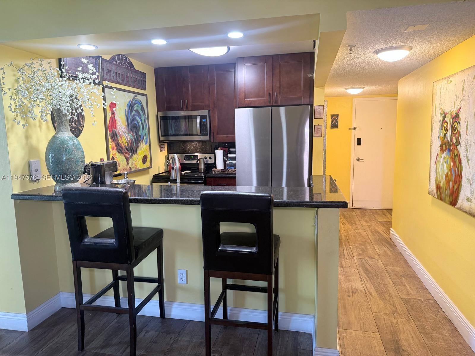 A kitchen features dark wood cabinets, stainless steel appliances, a granite breakfast bar, and yellow walls — 800 N Miami Ave # 609, Miami FL 33136, MIAMI, FL
