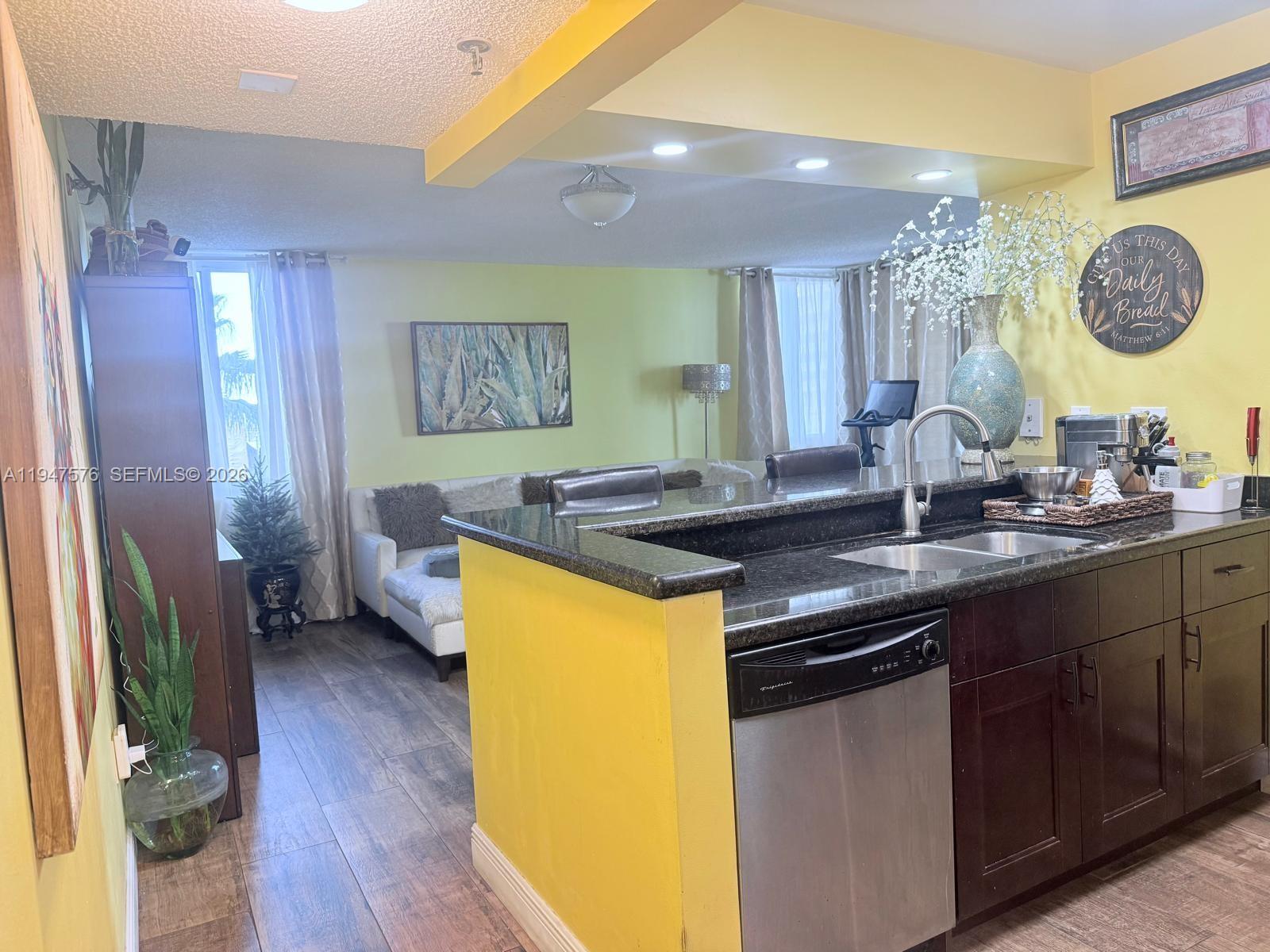 A kitchen with dark cabinets and granite countertops overlooks a living area with yellow walls — 800 N Miami Ave # 609, Miami FL 33136, MIAMI, FL
