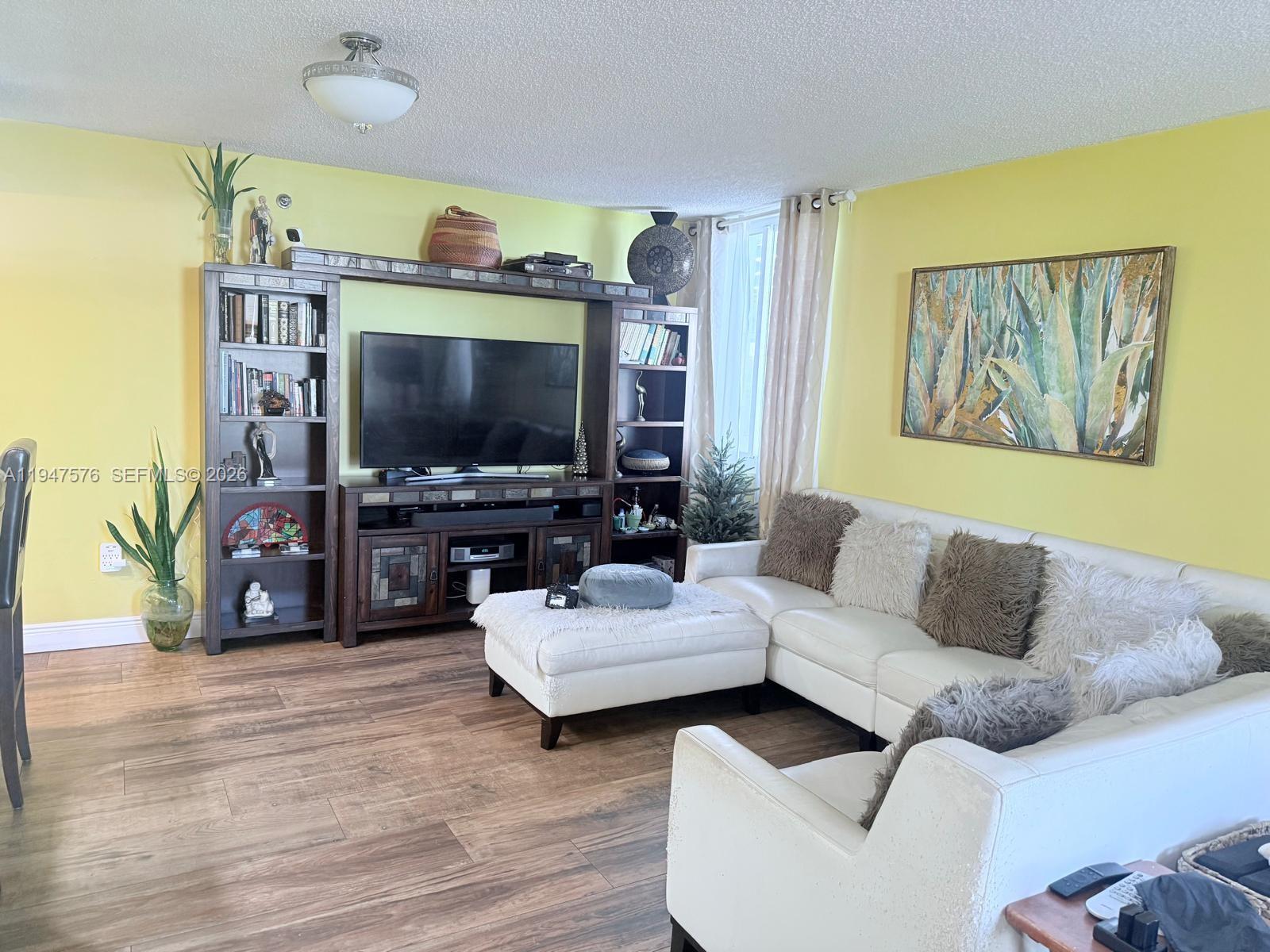 A living room features yellow walls, a large wooden entertainment center, and a white sectional — 800 N Miami Ave # 609, Miami FL 33136, MIAMI, FL