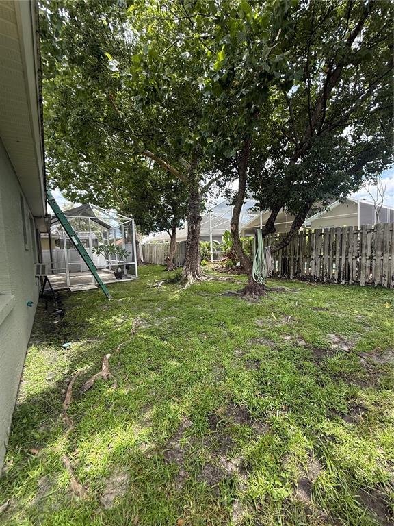 A backyard features a grassy lawn, two large trees, a wooden fence, and a screened enclosure — 2941 MAPLE GROVE PLACE, OVIEDO, FL