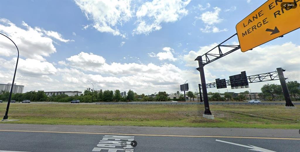 A view of a grassy roadside area with a highway sign and distant buildings — I-4, POLK CITY, FL