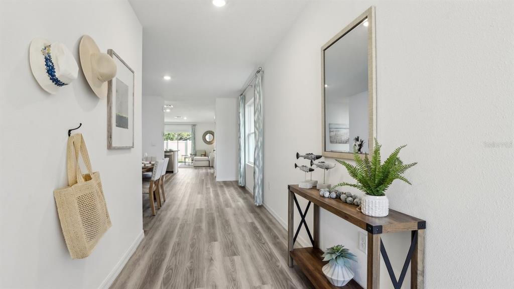 A bright entryway features wood-look flooring, a console table, and wall-mounted hats and decor — 32387 WEATHERED OAK DRIVE, WESLEY CHAPEL, FL