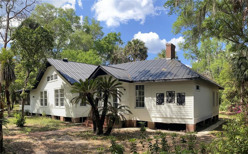 A white, single-story house with a dark metal roof sits in a wooded, grassy yard — 6015 QUAIL STREET, MELROSE, FL