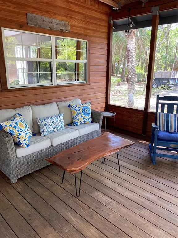 A screened-in wooden porch features a wicker sofa, a live-edge coffee table, and a rocking chair — 6015 QUAIL STREET, MELROSE, FL