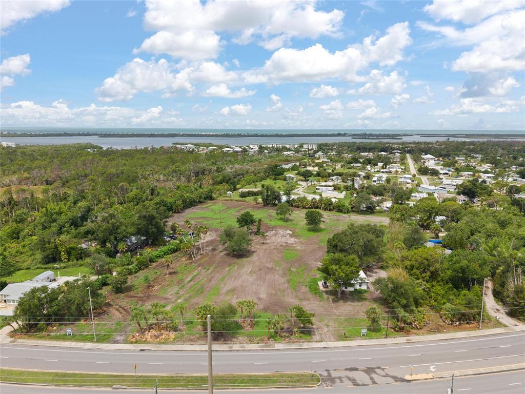 An aerial view shows a large, cleared vacant lot bordered by a road and trees — 5230 PLACIDA ROAD, ENGLEWOOD, FL