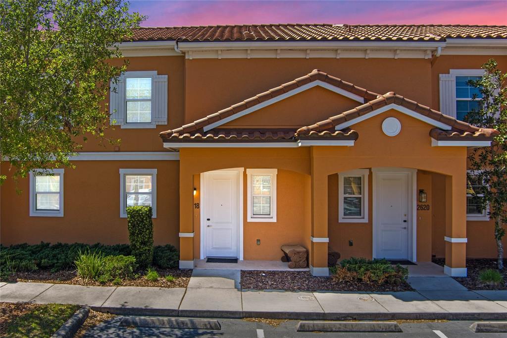 The exterior of a two-story tan townhouse features white trim, tiled roofs, and two entryways — 2618 ROADSTER LANE, KISSIMMEE, FL
