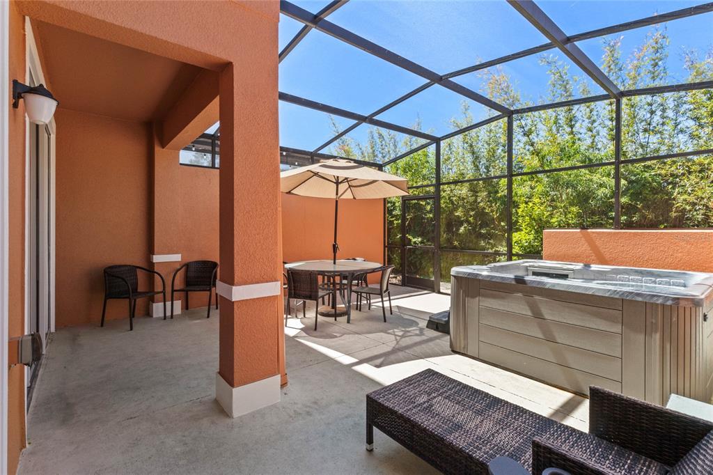 A screened-in patio features a hot tub, a dining set with an umbrella, and outdoor seating — 2618 ROADSTER LANE, KISSIMMEE, FL