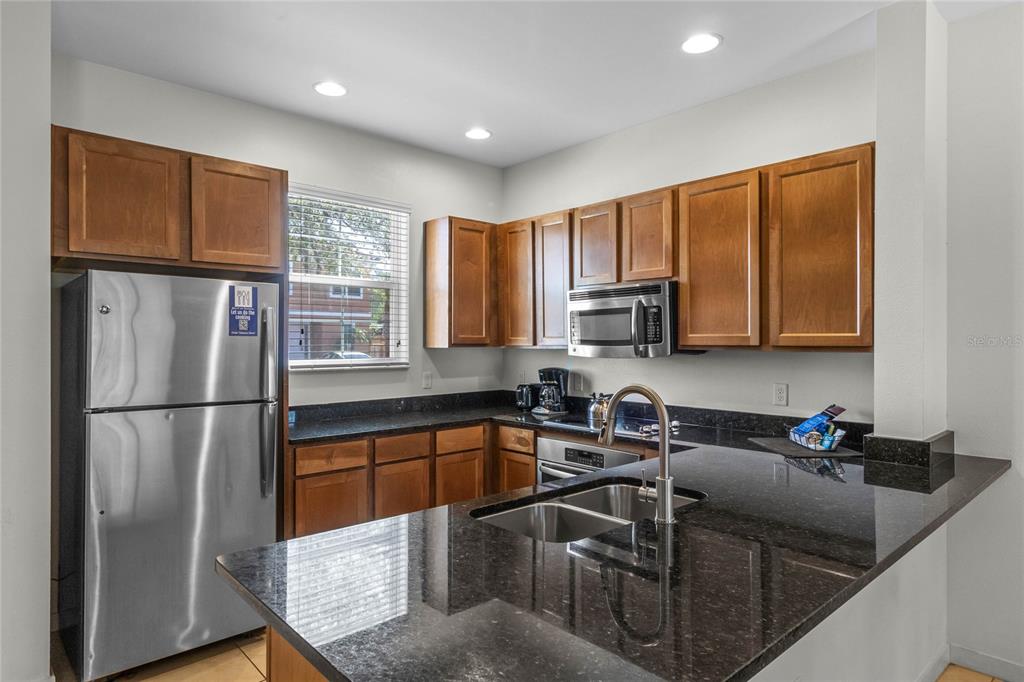 A kitchen features wood cabinets, dark granite countertops, stainless steel appliances, and a breakfast bar — 2618 ROADSTER LANE, KISSIMMEE, FL