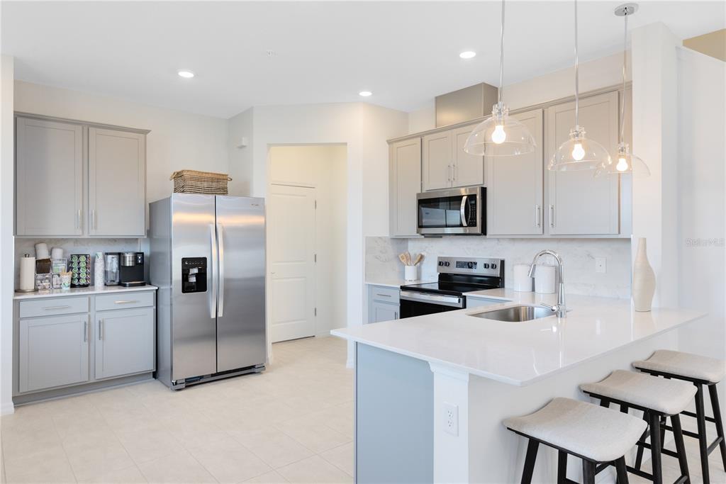 A modern kitchen features gray cabinets, stainless steel appliances, a white island, and pendant lighting — 4401 JETTY LANE NE, PALM BAY, FL