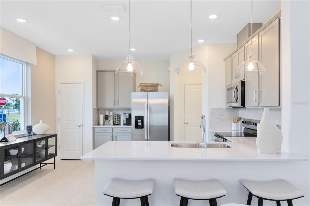 A modern kitchen features white countertops, stainless steel appliances, and three gray bar stools — 4401 JETTY LANE NE, PALM BAY, FL