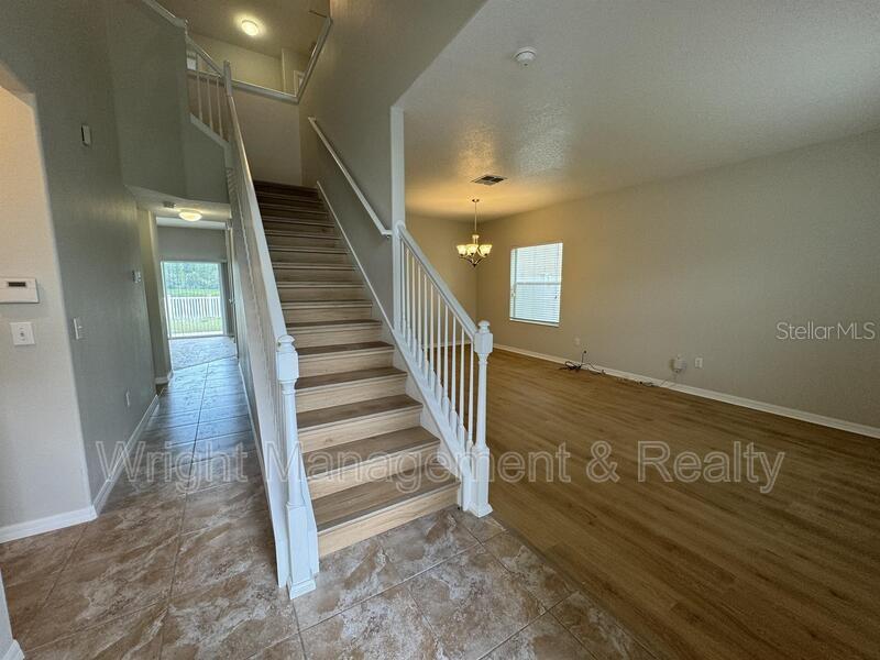 A staircase with wood treads and white railings sits between a tiled entryway and living area — 3627 MORGONS CASTLE COURT, LAND O LAKES, FL