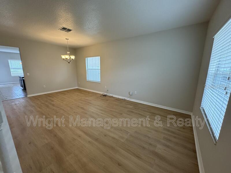 An empty living room features light wood-look flooring, beige walls, and a hanging light fixture — 3627 MORGONS CASTLE COURT, LAND O LAKES, FL