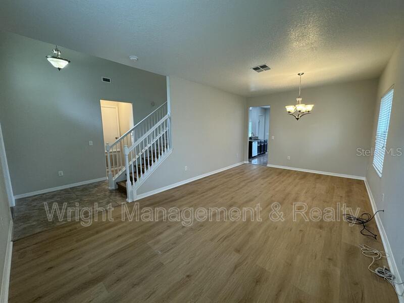 An open living area features light wood-look flooring, a staircase, and a dining room chandelier — 3627 MORGONS CASTLE COURT, LAND O LAKES, FL