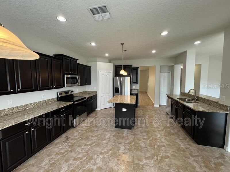 A kitchen features dark wood cabinets, granite countertops, a center island, and tile flooring — 3627 MORGONS CASTLE COURT, LAND O LAKES, FL