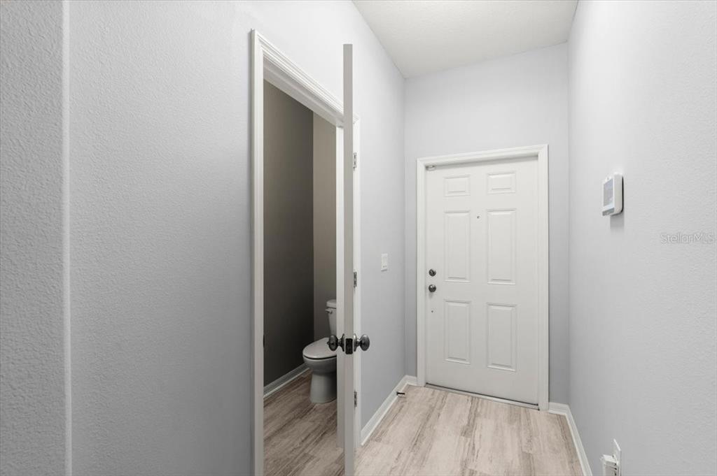 A hallway with light wood-look flooring leads to a white door and a small bathroom — 107 WENTWORTH GRANDE DRIVE, DAYTONA BEACH, FL