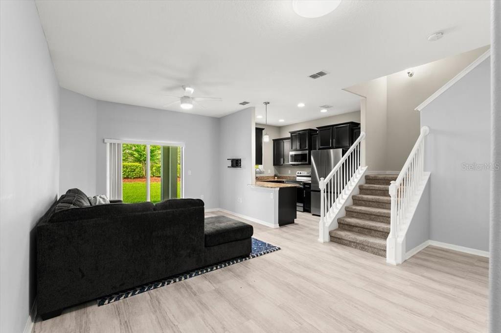 A living room with light flooring, a dark sectional sofa, and stairs leading to a kitchen — 107 WENTWORTH GRANDE DRIVE, DAYTONA BEACH, FL