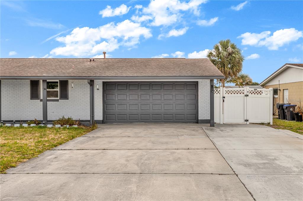 A gray brick house features a dark gray garage door and a white vinyl fence — 5195 SHARLENE DRIVE, TITUSVILLE, FL