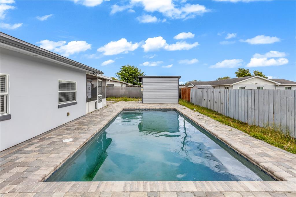 A rectangular swimming pool sits in a paved backyard next to a house and shed — 5195 SHARLENE DRIVE, TITUSVILLE, FL