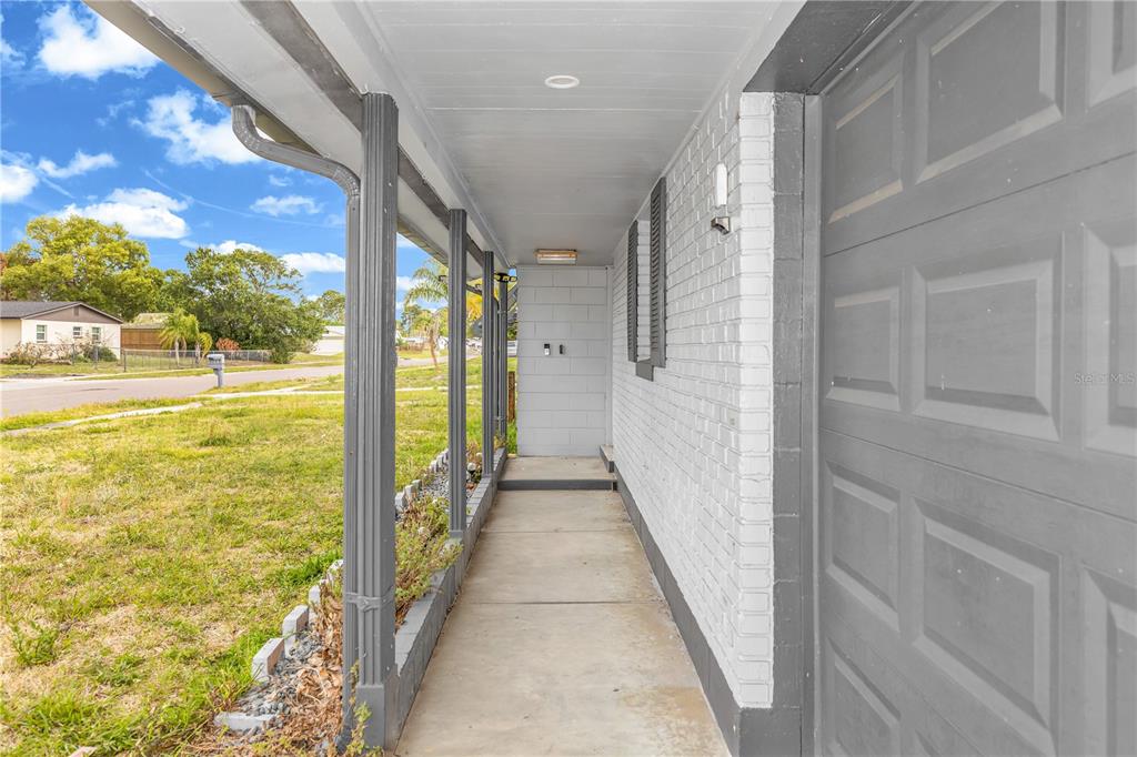 A covered concrete walkway runs along the side of a house with a gray garage door — 5195 SHARLENE DRIVE, TITUSVILLE, FL