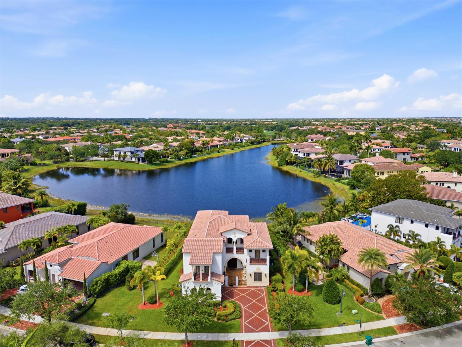 An aerial view shows a large house with a tiled roof beside a lake — 8289 Emerald Avenue, Parkland FL 33076, PARKLAND, FL