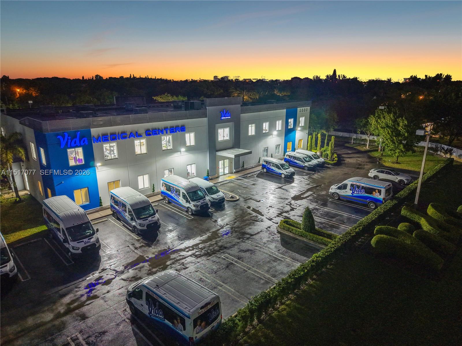 An aerial view shows a two-story medical center building with several branded vans in the parking lot — 2550 NW 100th Ave, Doral FL 33172, DORAL, FL