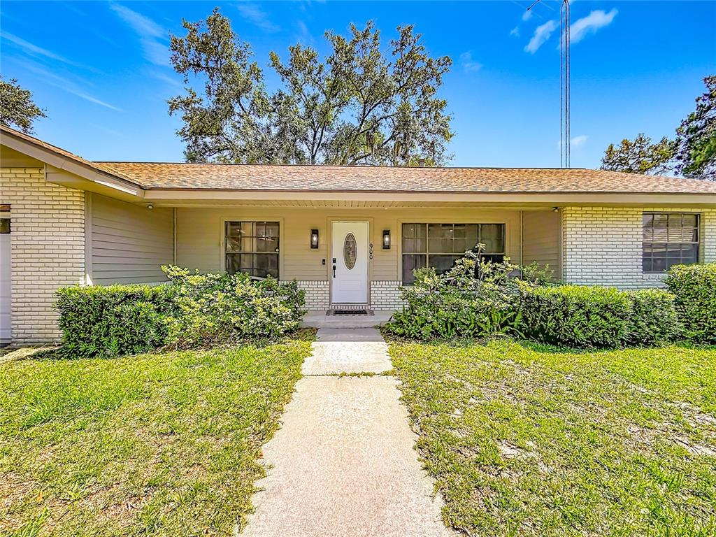A single-story house with a white brick facade, a centered front door, and manicured landscaping — 900 NE 165TH STREET, CITRA, FL