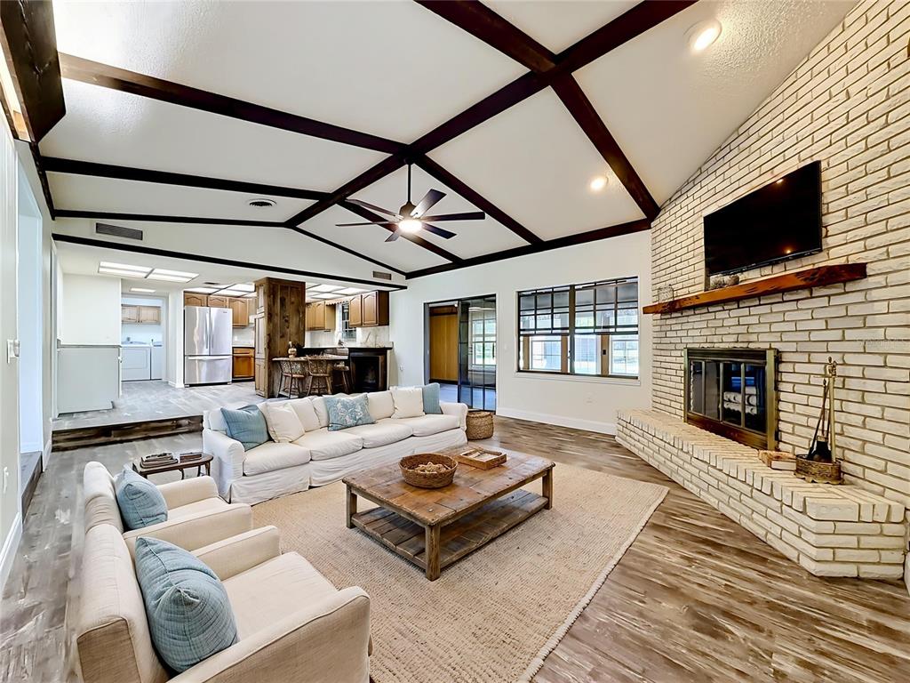 A living room features a vaulted ceiling with exposed beams, a brick fireplace, and wood-look flooring — 900 NE 165TH STREET, CITRA, FL