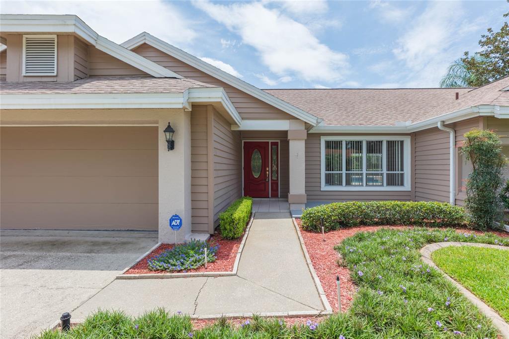 A tan house exterior features a red front door, a concrete walkway, and red mulch — 1405 OXFORDSHIRE COURT, BRANDON, FL
