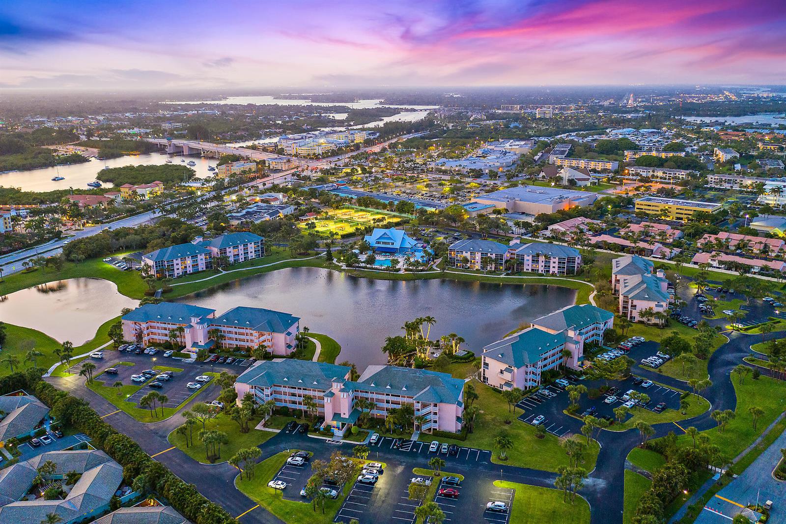 An aerial view shows a multi-building apartment complex surrounding a lake at sunset — 353 S Us Highway 1 # A107, Jupiter FL 33477, JUPITER, FL