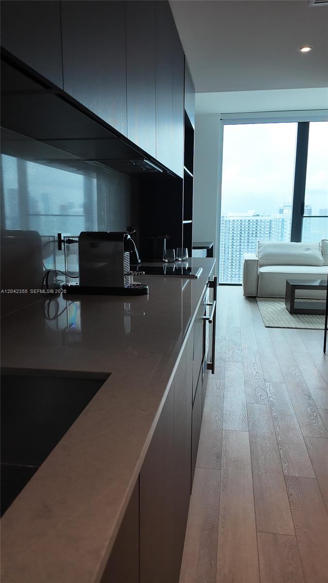 A modern kitchen with dark cabinetry and light countertops overlooks a living area and city — 20 NE 11th St, Miami FL 33132, MIAMI, FL