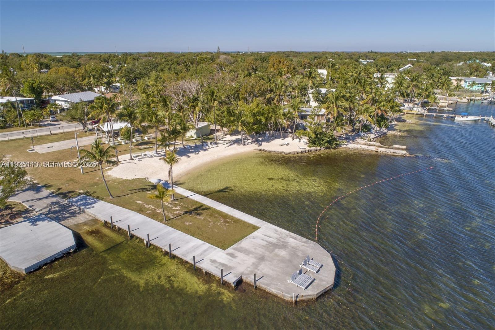An aerial view shows a concrete pier extending into the water near a sandy beach — 29 Bonefish Ave, Key Largo FL 33037, KEY LARGO, FL