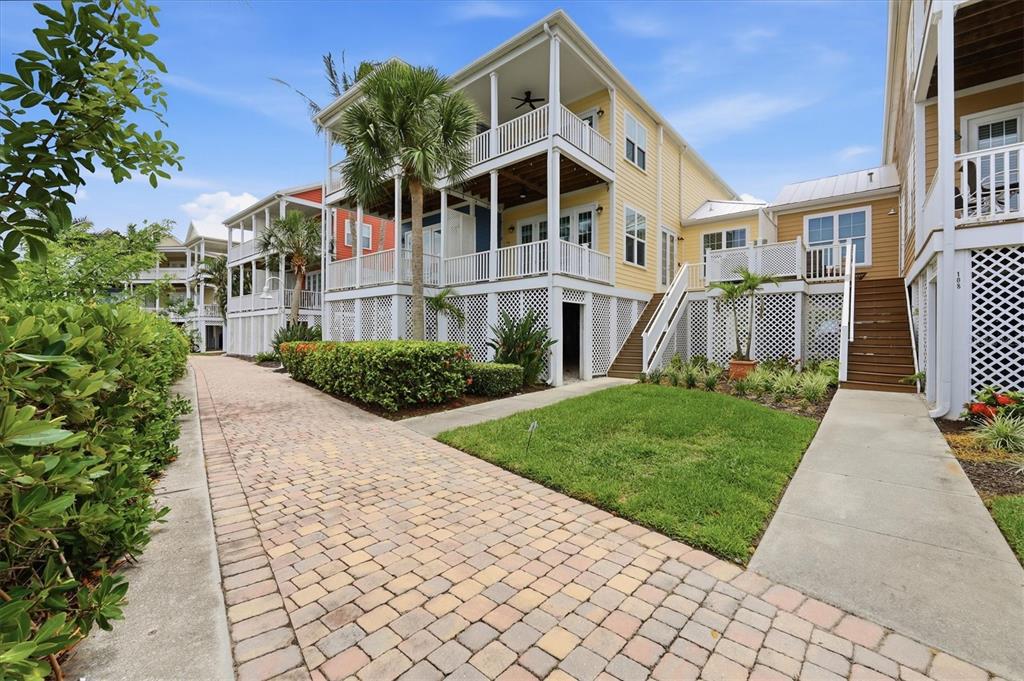 A yellow multi-story house with elevated porches sits beside a brick walkway and lawn — 11780 ANGLERS CLUB DRIVE UNIT 107, PLACIDA, FL