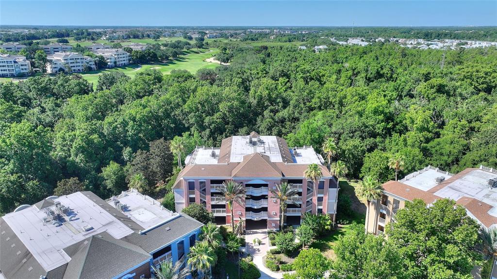 An aerial view shows a multi-story apartment building surrounded by lush trees and nearby golf courses — 7656 WHISPER WAY UNIT 402, REUNION, FL