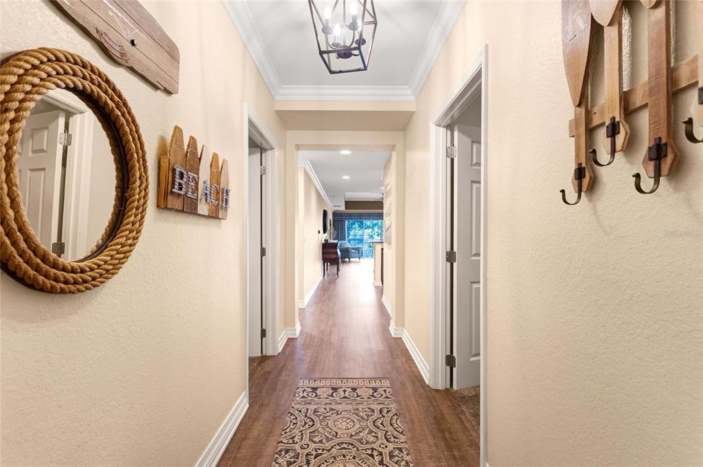 A hallway with light walls, wood-look flooring, a patterned runner, and coastal-themed wall decor — 7656 WHISPER WAY UNIT 402, REUNION, FL