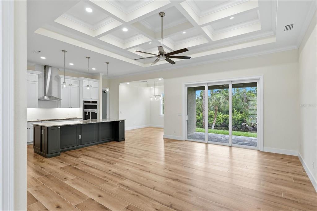 A modern kitchen and living area featuring a coffered ceiling, dark island, and sliding doors — 2649 SIMONTON AVENUE, NORTH PORT, FL