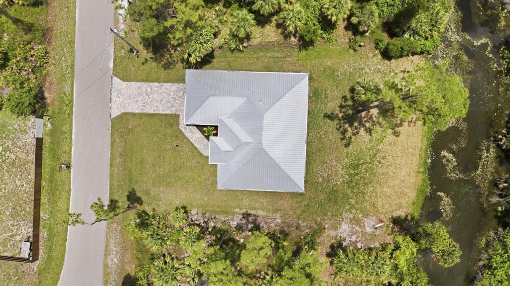 An aerial view shows a house with a metal roof, driveway, and yard near water — 2649 SIMONTON AVENUE, NORTH PORT, FL